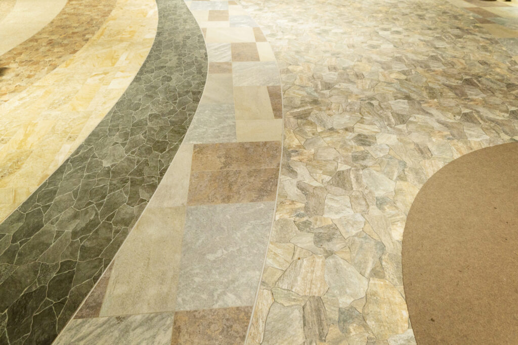 Hand holding a stone tile sample above patterned mosaic tiles